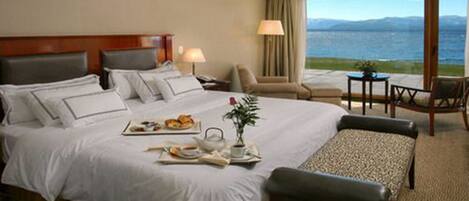 Habitación de hotel con una cama grande, una mesa de comedor con desayuno, una silla y vista al mar.