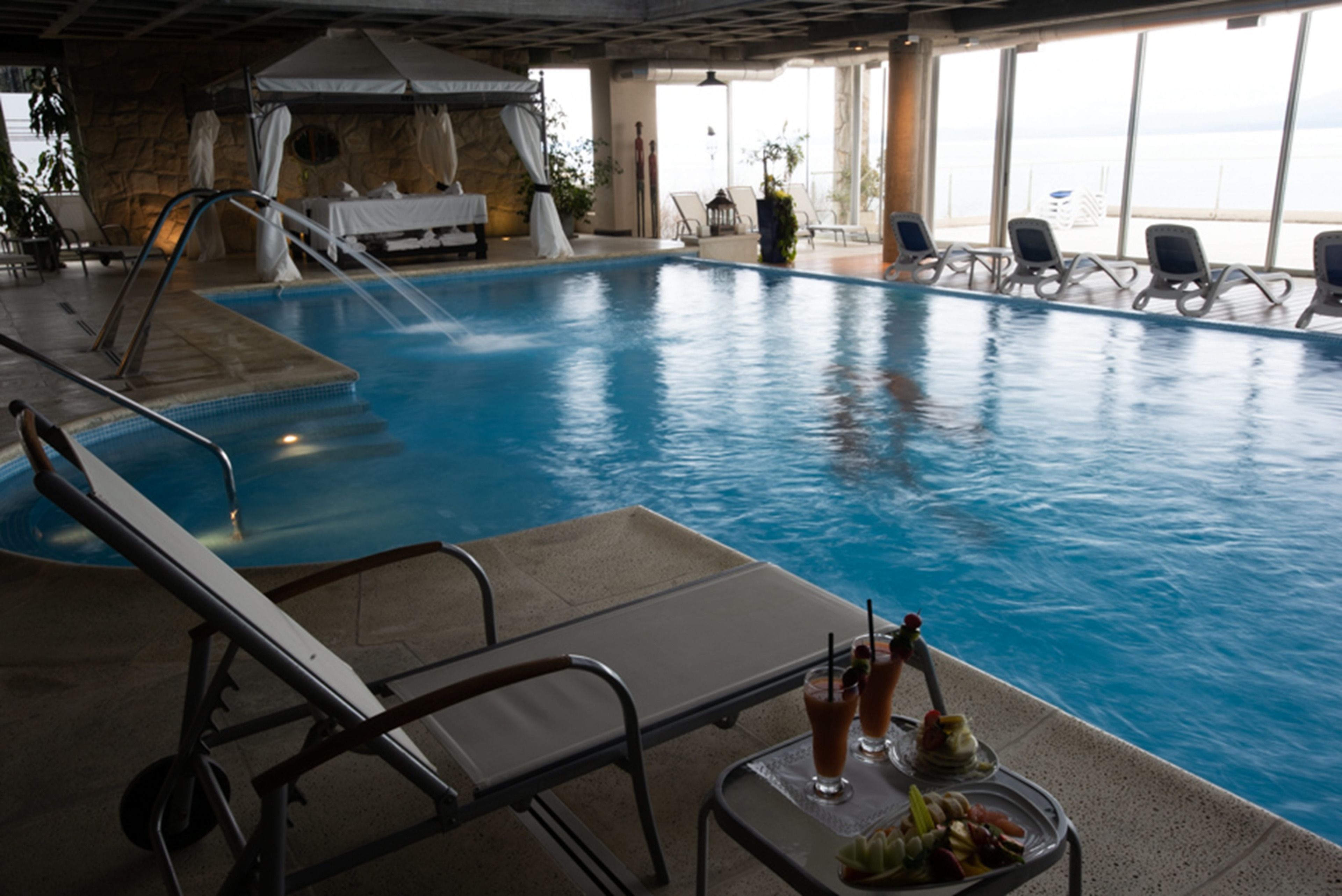 Una piscina interior con sillones de descanso y una mesa con bebidas.