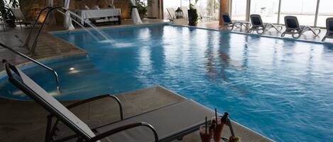 Una piscina interior con sillones de descanso y una mesa con bebidas.