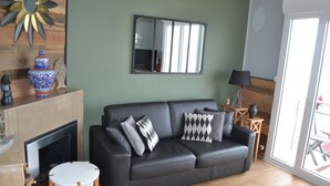 A living room with a black leather sofa, a fireplace, a mirror, and a view through a glass door.