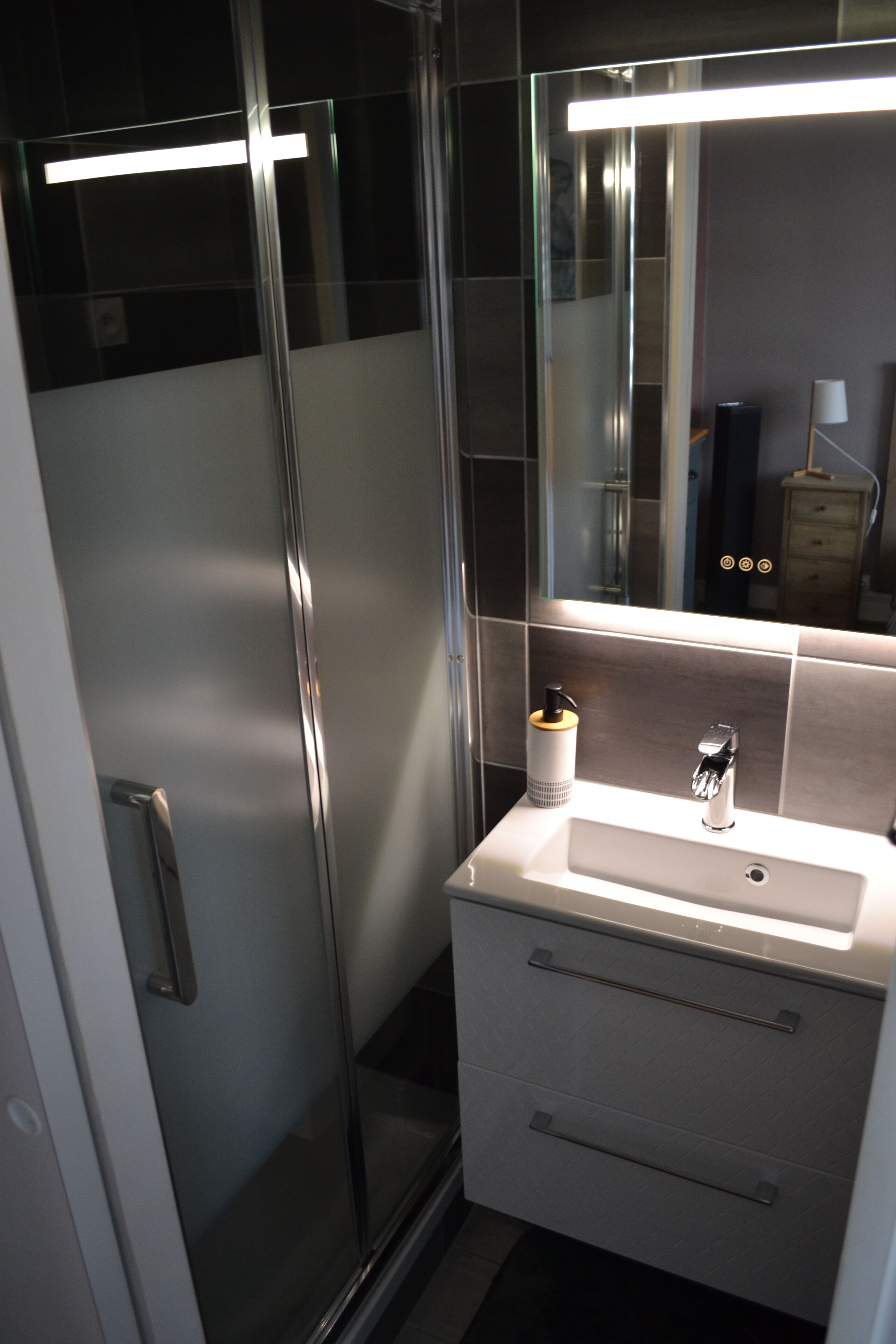 A modern bathroom with a glass shower enclosure, a white sink with a mirror above it, and a small vanity with drawers.