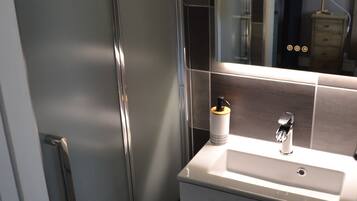 A modern bathroom with a glass shower enclosure, a white sink with a mirror above it, and a small vanity with drawers.