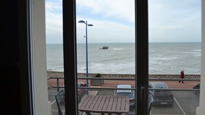 A view from a balcony overlooking a beach with a stone wall, a street lamp, and parked cars.