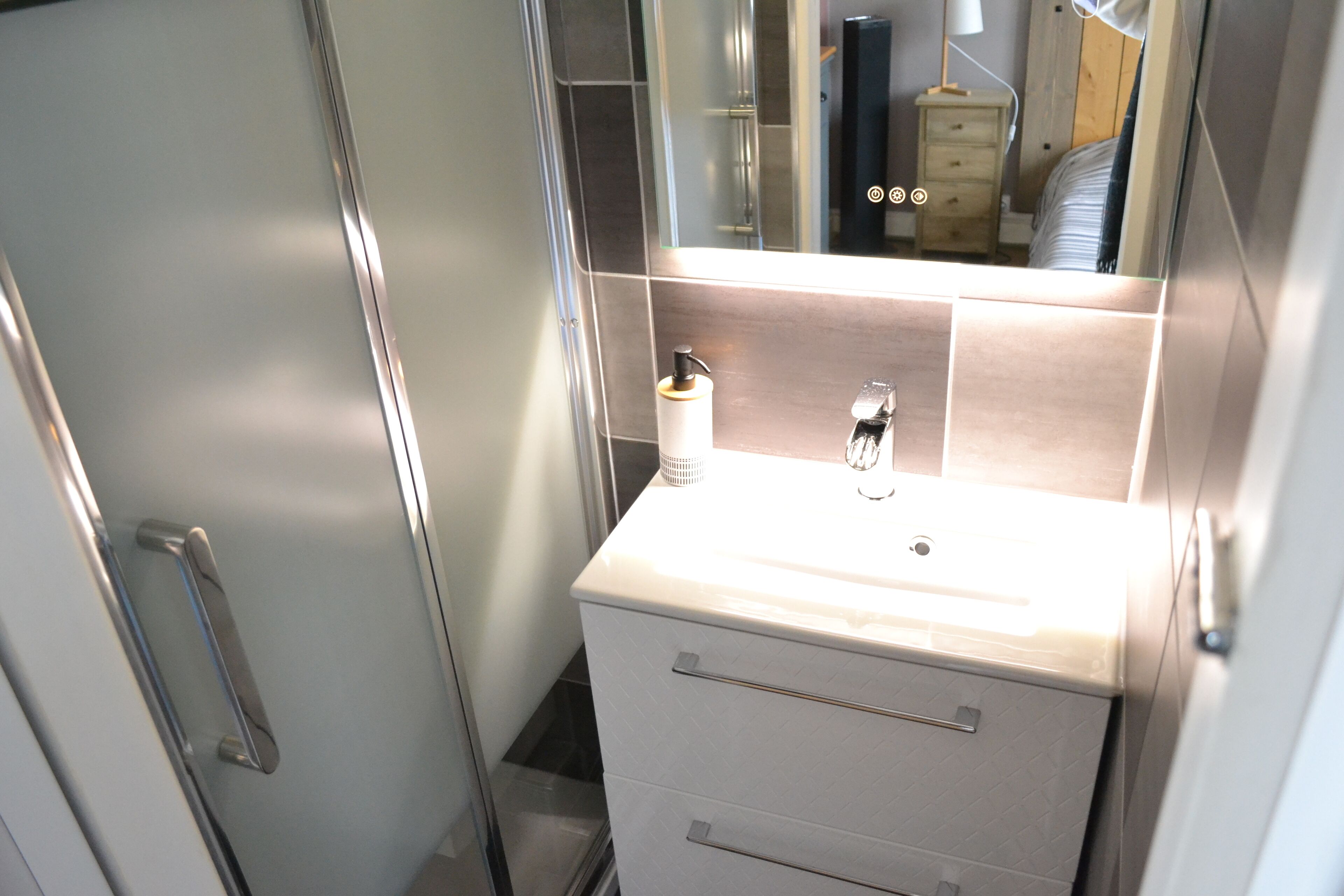 Een badkamer met een witte wastafel, een spiegel en een zeepdispenser.