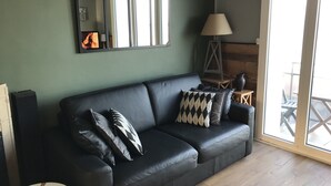 A black leather sofa with patterned cushions, a mirror, a lamp, and a wooden floor.