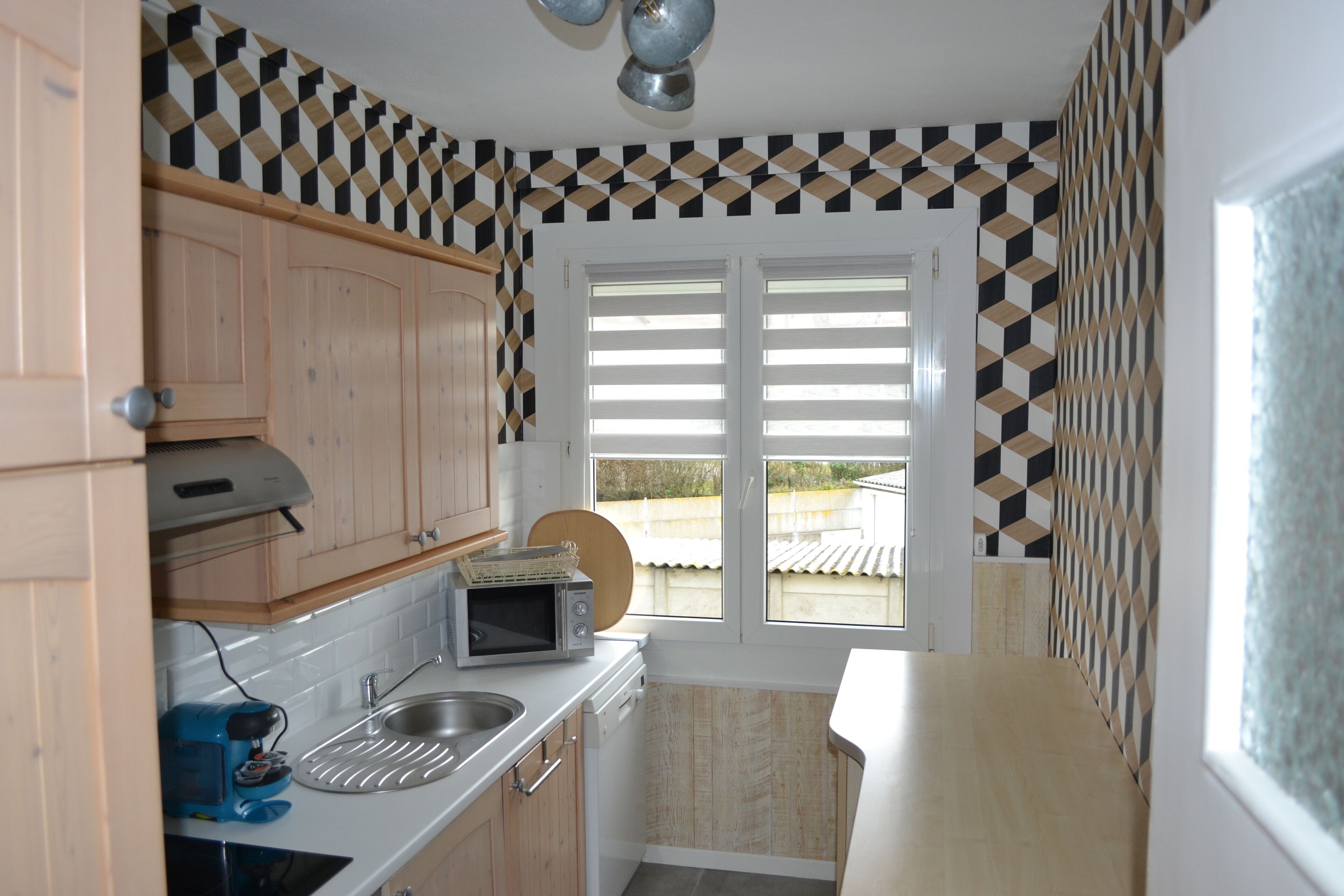 A compact kitchen with wooden cabinets, a microwave, a sink, and a window with blinds.