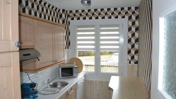 A compact kitchen with wooden cabinets, a microwave, a sink, and a window with blinds.
