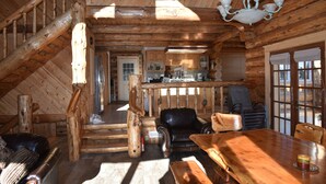 A log cabin interior with a wooden staircase, a dining area, a kitchen, and a living room with a fireplace. - Log home On the Deschutes River Bend, OR (Bend)