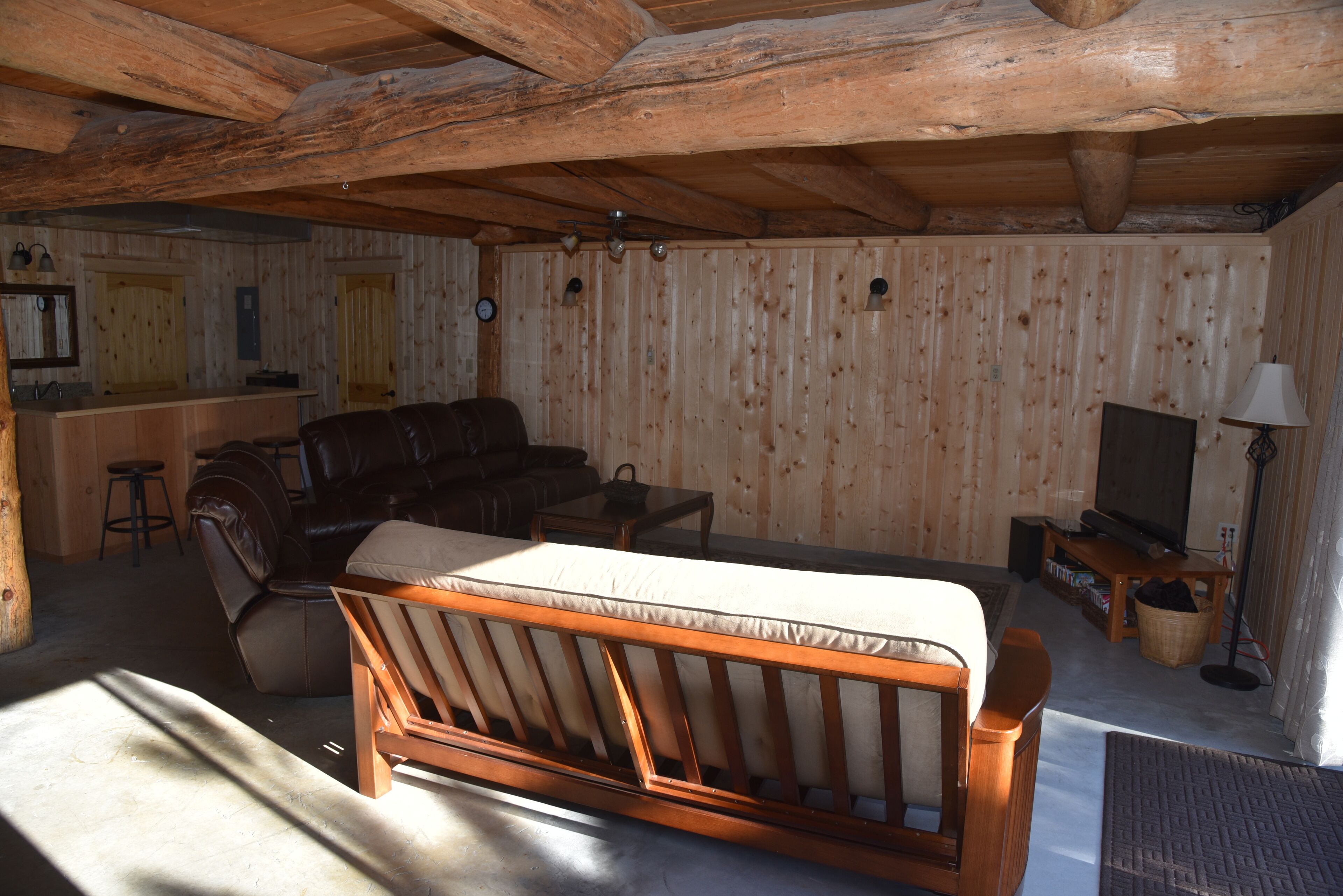 Interior de una cabaña de troncos con una cama de madera, un sofá de cuero, una mesita y un televisor.