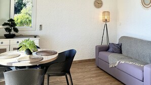 Un salon moderne comprenant un canapé, une table à manger avec des chaises, un luminaire suspendu, une horloge murale et un appareil de climatisation.