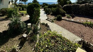 Un chemin menant à une maison offrant une vue sur la mer, entourée de jardins bien entretenus et sous un ciel dégagé.