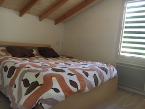A bedroom with a bed, wooden beams, a window with blinds, and a radiator.