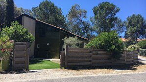 A rustic wooden cabin with a metal roof, surrounded by a wooden fence and lush greenery. - BEAUTIFUL VILLA WITH HEATED JACUZZI AND WIFI, facing the golf course in Lacanau-Océan; sleeps 6, 3 bedrooms, 2 bathrooms (Lacanau)