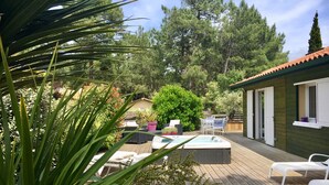 A wooden deck with outdoor seating, a hot tub, and a small building with windows. - BEAUTIFUL VILLA WITH HEATED JACUZZI AND WIFI, facing the golf course in Lacanau-Océan; sleeps 6, 3 bedrooms, 2 bathrooms (Lacanau)