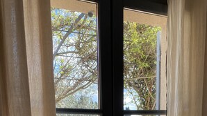 A view through a glass door with a metal handle, leading to a backyard with a swimming pool, a wooden deck, and a metal fence.