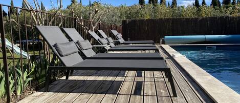Um deck de madeira com cadeiras de lounge e uma piscina.