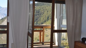 A room with a large window offering a view of a forested mountain range. - Charming apartment 40 m2 / 4 p classified 3 *** old district Alpe, magnificent view (Huez)