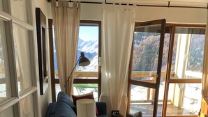 A cozy living room with a blue sofa, a small table, and a view of mountains through large windows. - Charming apartment 40 m2 / 4 p classified 3 *** old district Alpe, magnificent view (Huez)