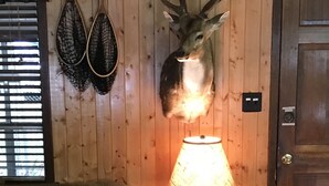 Une pièce avec un mur en bois, une tête de cerf accrochée au mur, une table avec une lampe et un canapé vert.