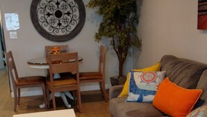 A living room with a white table, a grey sofa with colorful cushions, a wooden dining table with chairs, and a decorative wall piece. - Ocean Front Condo - 1 Bedroom/bath - Sleeps 4 (Lincoln City)