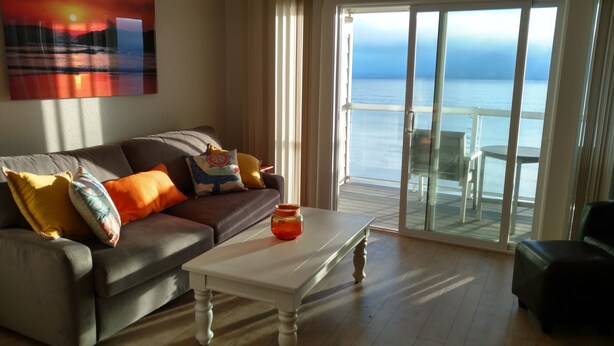 A living room with a sofa, colorful cushions, a white coffee table, and a view of the sea through large glass doors. - Ocean Front Condo - 1 Bedroom/bath - Sleeps 4 (Lincoln City)