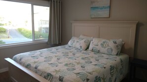 A bedroom with a bed, a window with a view of a road and greenery, and a painting on the wall. - Ocean Front Condo - 1 Bedroom/bath - Sleeps 4 (Lincoln City)