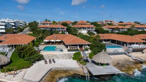 Ein Resort mit mehreren Gebäuden, einem Pool und einem Steg, der ins Meer führt.
