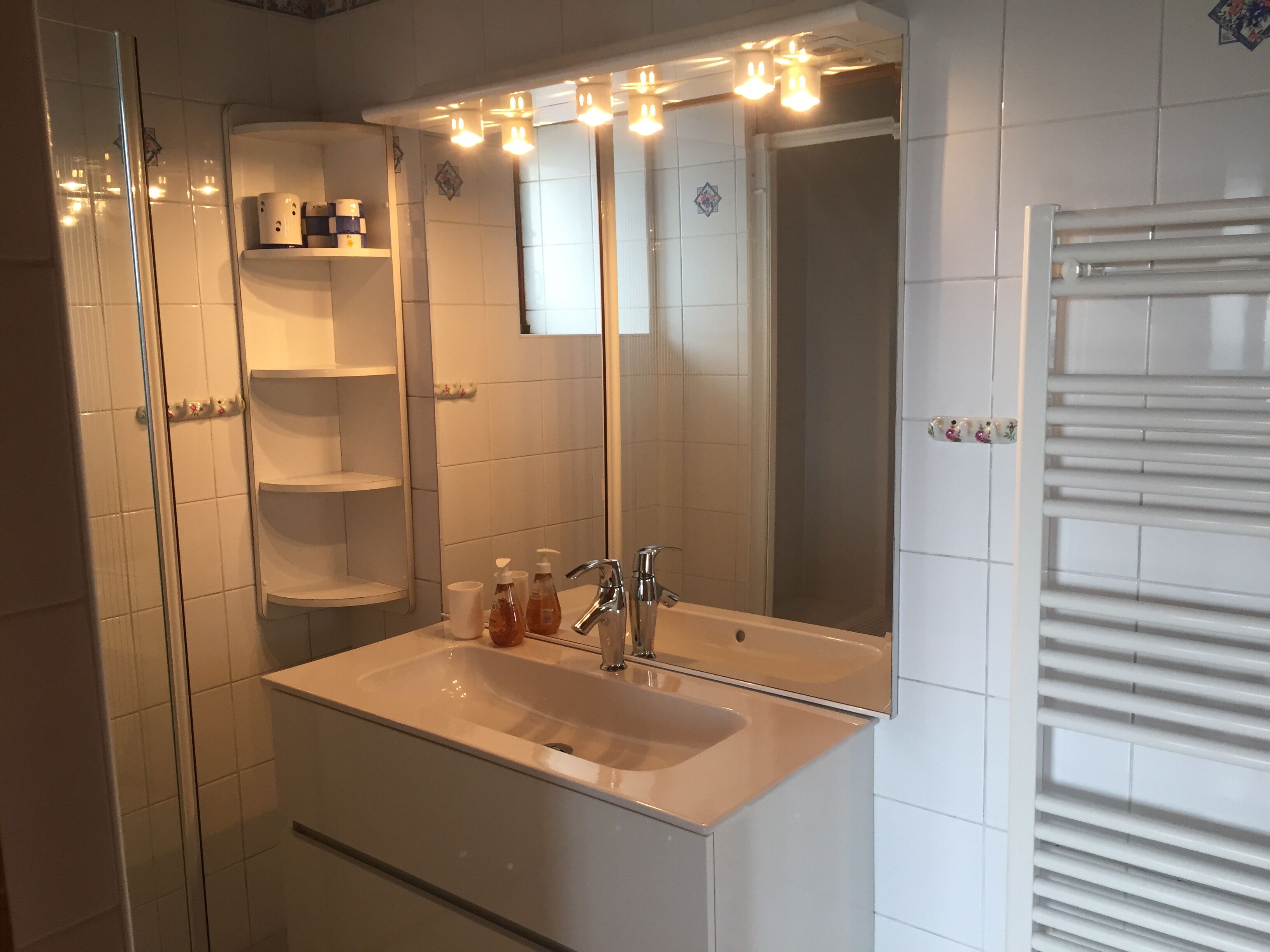 A bathroom with a white sink, a mirror, and a shower. There are shelves above the sink and a towel rack on the wall.