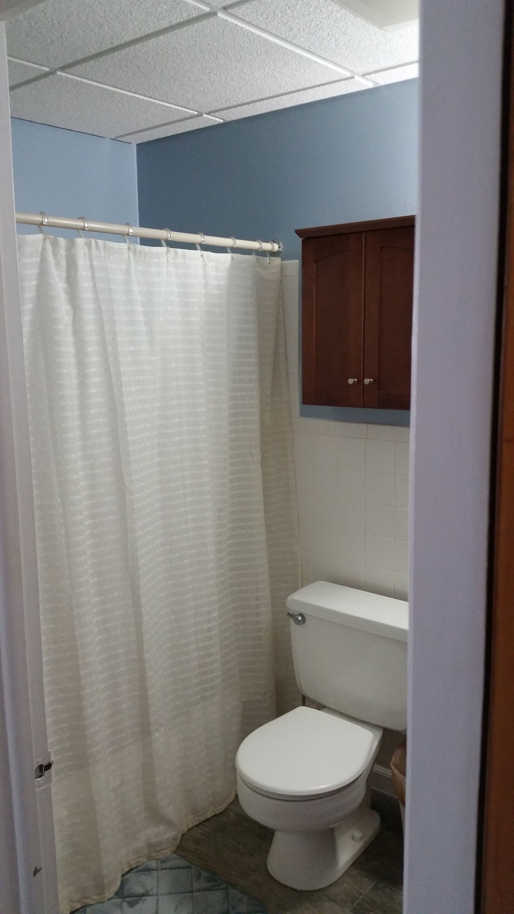 A bathroom with a white toilet, a shower curtain, and a wooden cabinet above the toilet.
