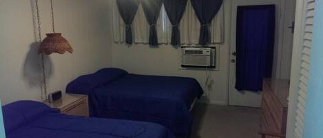 Quarto com duas camas, uma luminária pendente, um aparelho de ar condicionado e uma porta com cortina.