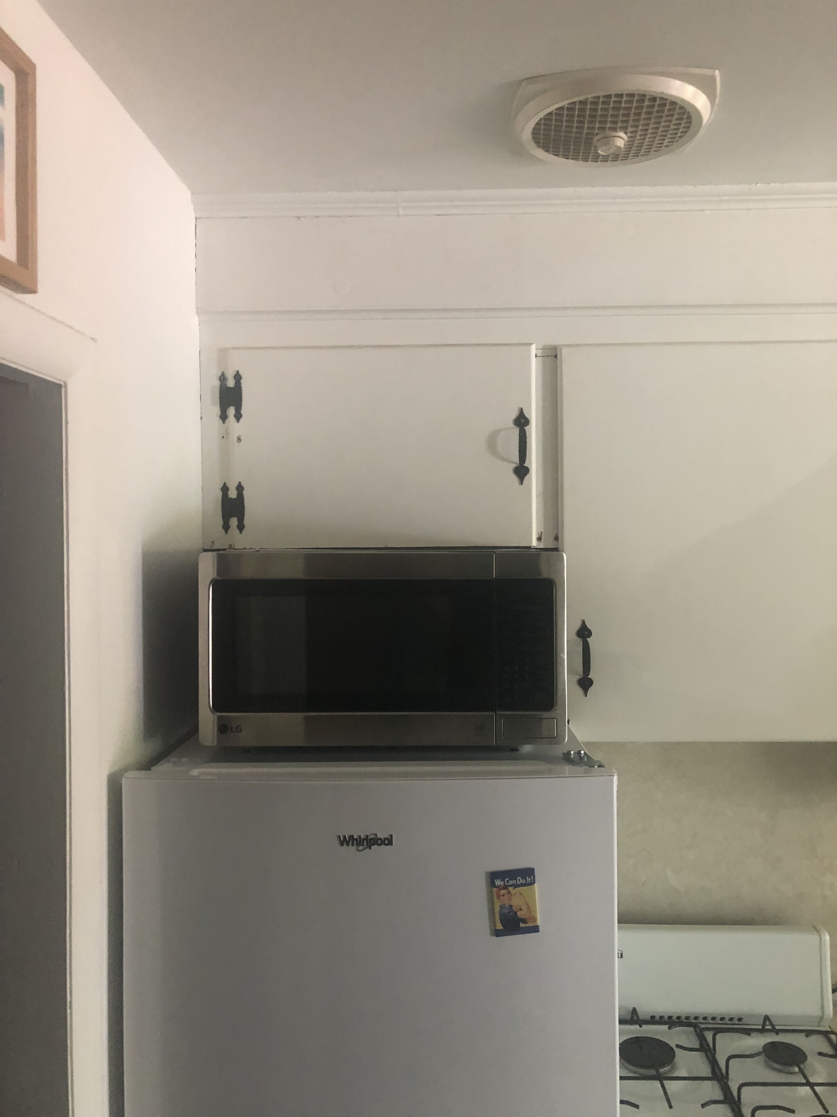 Una cocina con un refrigerador Whirlpool blanco, un microondas encima y una estufa a gas.
