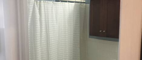 Une salle de bain avec un rideau de douche, des toilettes et un meuble.