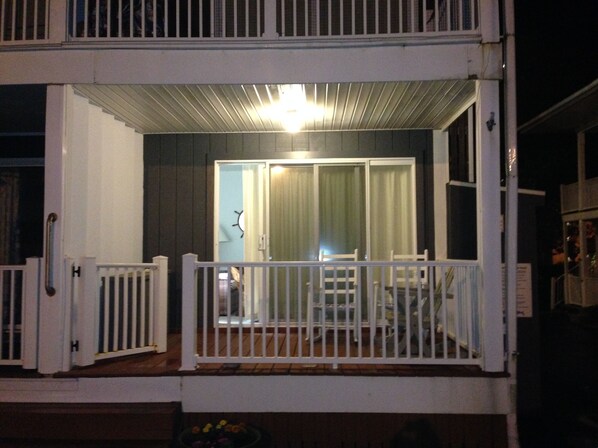 A covered outdoor area with a white railing, a door leading inside, and a light fixture above.