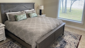 Quarto com cama, mesas de cabeceira, luminária, janela com persianas e um tapete estampado.