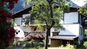 Ein Haus mit einer Stein-Fassade, einer Holzterrasse und einem Kiesweg, der zum Eingang führt.