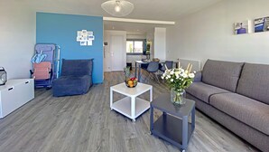A modern living room with a grey sofa, a white coffee table, and a blue accent wall. - Spacious studio with terrace, sea and shops 700m, private parking, Wi-Fi included (Larmor-Plage)