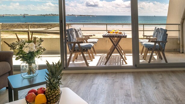 A balcony with a table set for breakfast, chairs, and a view of the beach and ocean. - Spacious studio with terrace, sea and shops 700m, private parking, Wi-Fi included (Larmor-Plage)
