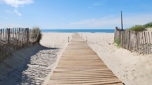 A wooden boardwalk leading to a sandy beach with a clear blue sky.