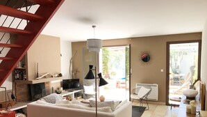 A living room with a sofa, TV, and a fireplace. There is a staircase on the left and a door leading to a balcony.