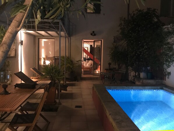 Un área de piscina al aire libre con sillones reclinables, una mesita y plantas en macetas.