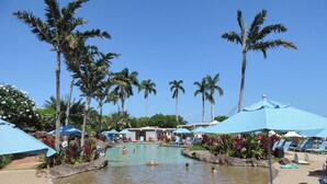 Un espace aménagé au bord de la piscine, avec des chaises longues et des parasols, entouré de palmiers.