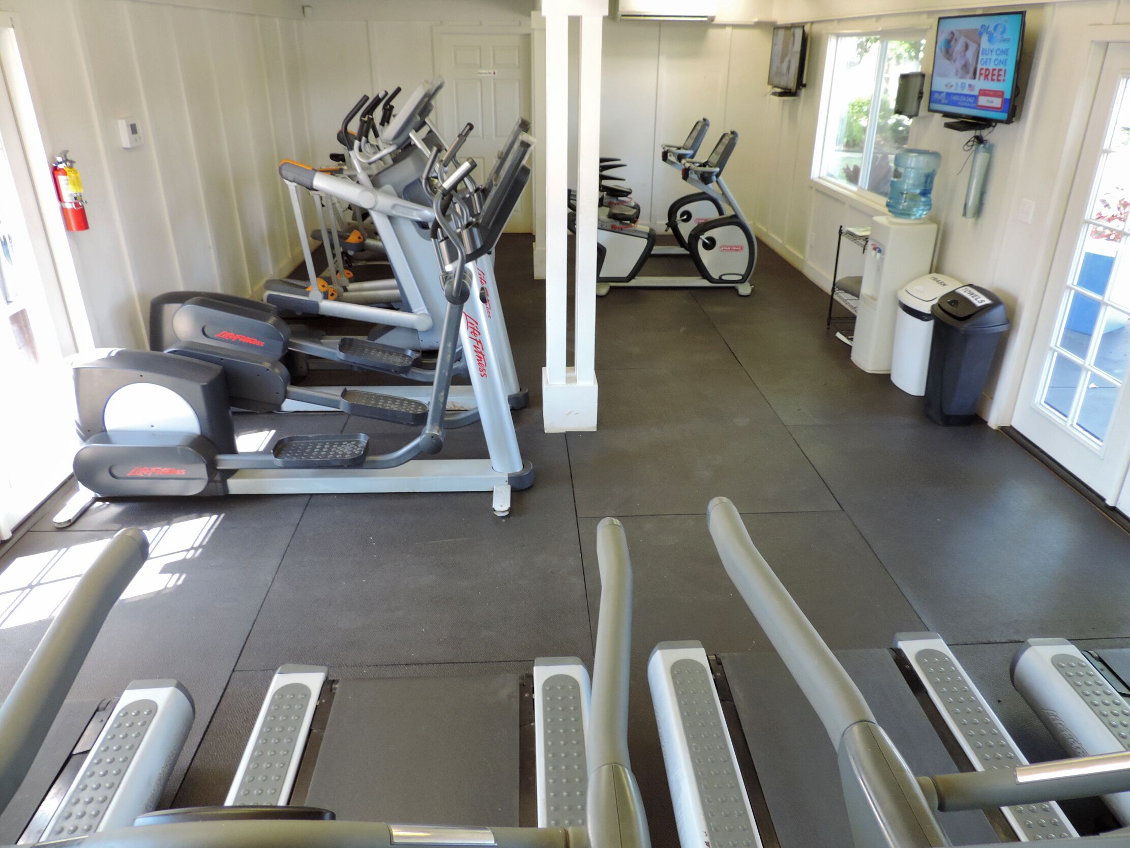 A gym with multiple treadmills, a water dispenser, and a TV on the wall.