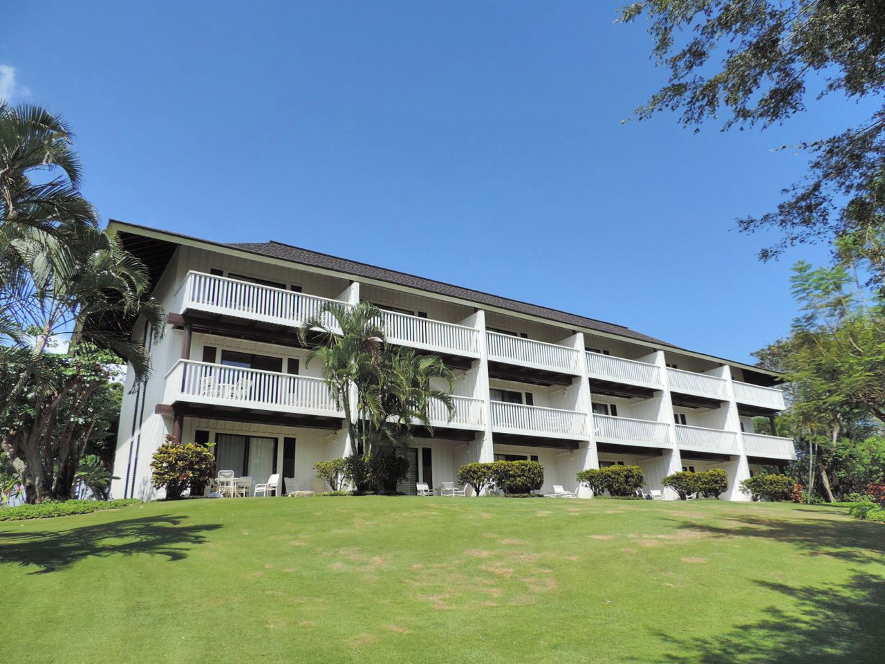 A multi-story hotel with a flat roof, white balconies, and a well-maintained lawn.