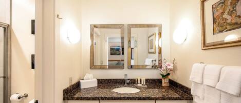 Une salle de bain avec un double lavabo, deux miroirs, des toilettes et un tableau encadré au mur.