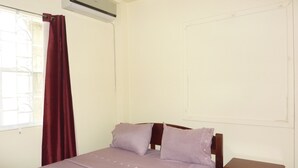 Ein Einzelbett mit Holzrahmen, ein kleiner Nachttisch und ein Fenster mit Vorhang.