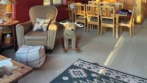 Un salon spacieux avec un plafond haut, des meubles en bois et une grande fenêtre équipée de stores.