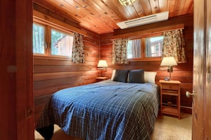 A wooden cabin bedroom with a bed, two bedside tables with lamps, and a window with curtains.