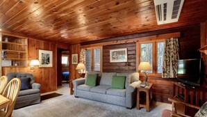 A cozy cabin interior with a wooden ceiling, a sofa, a television, and a dining area.