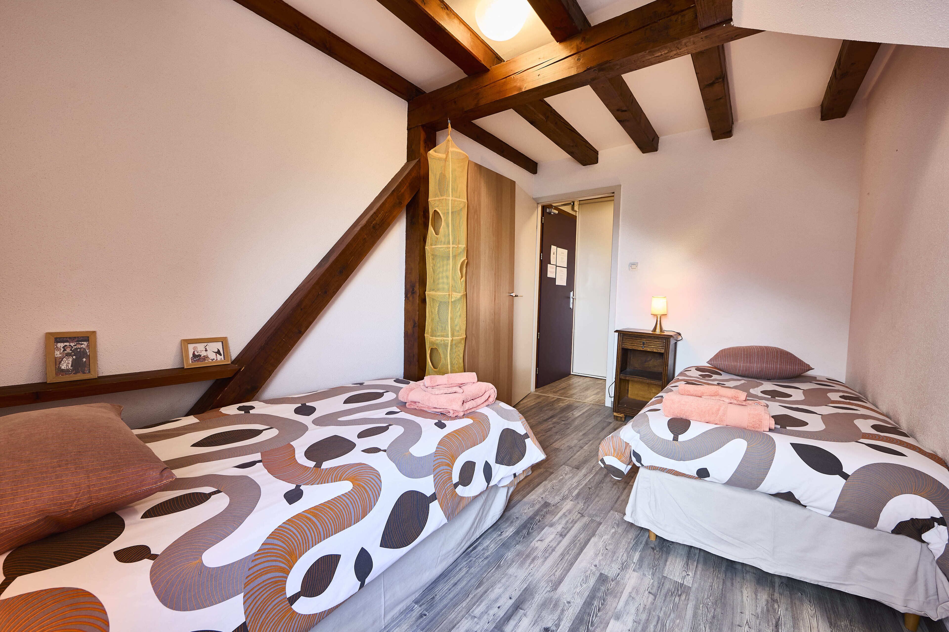 Un dormitorio con dos camas, vigas de madera, una puerta de madera y una mesita de noche con lámpara.