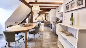 Un comedor con una mesa y sillas de madera, una lámpara colgante y una cocina al fondo.
